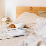 Comforting breakfast setup with coffee, pastry, and a notebook in a cozy bed environment.